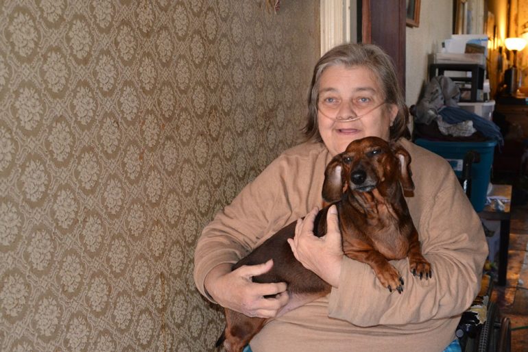 Dawn Ford sits in a first-floor hallway with her dog, Sarge, who catches the mice that come into her South Smallwood Street home. (Capital News Service photo by Abby Mergenmeier)