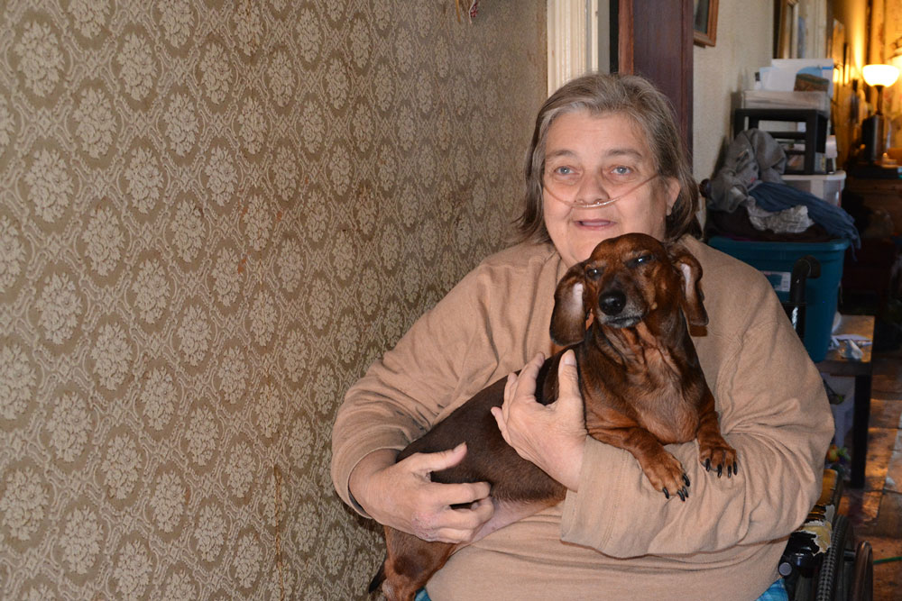 Dawn Ford sits in a first-floor hallway with her dog, Sarge, who catches the mice that come into her South Smallwood Street home. (Capital News Service photo by Abby Mergenmeier)