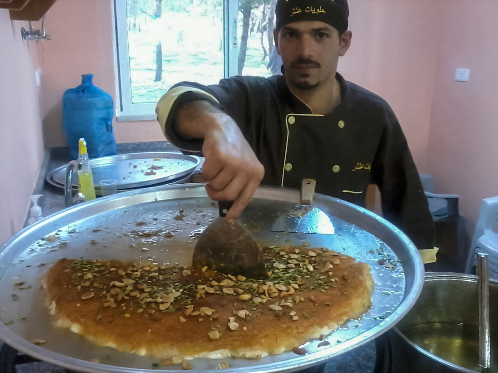 Nour cutting into kanafeh while working at a dessert shop in Jordan (Photo courtesy of Nour).
