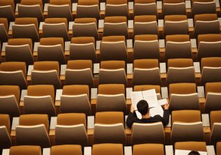 A lone student sitting in a lecture seat from bird's eye view.