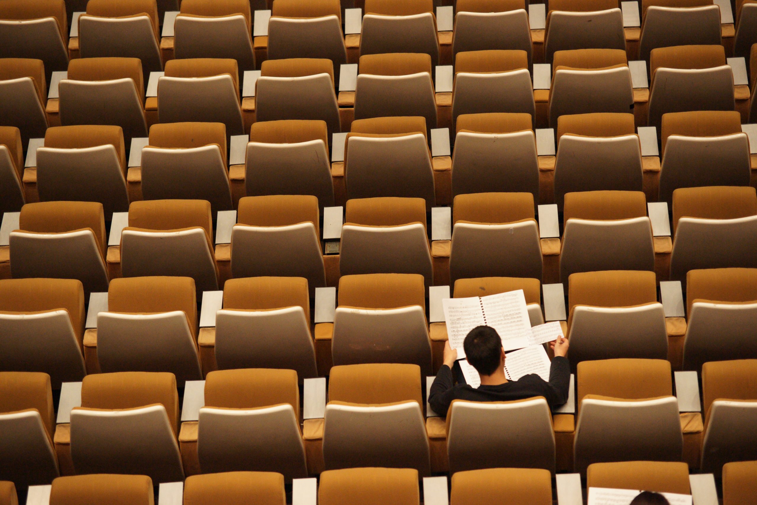A lone student sitting in a lecture seat from bird's eye view.