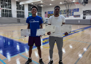 Clarence “Ray” Askins (left), 17, and Kristopher Mitchell (right), 17, show off their 4.0 GPA certificates in the gym of the REACH! Partnership school. Photo by Victoria Vandergriff/Capital News Service