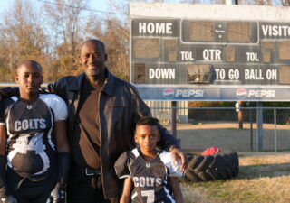 Ronald Redmond (center) stands on a football field in Lexington, Mississippi, where his sons, 11-year-old R.J. (left) and seven-year-old Mason (right), play for the Lexington Colts youth football team. Photo by Jenna Bloom/University of Maryland.
