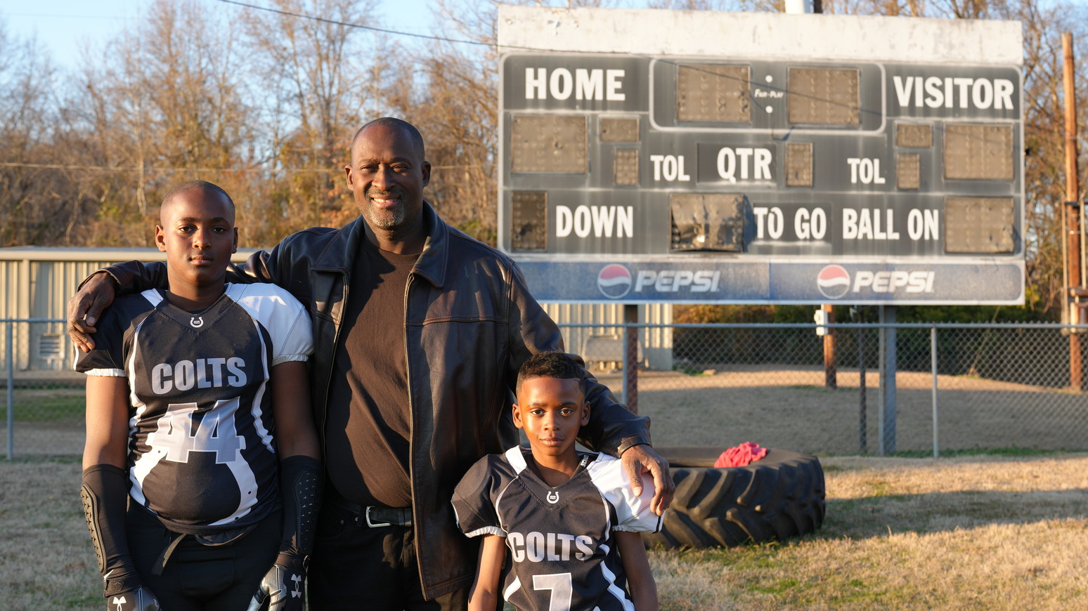 Ronald Redmond (center) stands on a football field in Lexington, Mississippi, where his sons, 11-year-old R.J. (left) and seven-year-old Mason (right), play for the Lexington Colts youth football team. Photo by Jenna Bloom/University of Maryland.