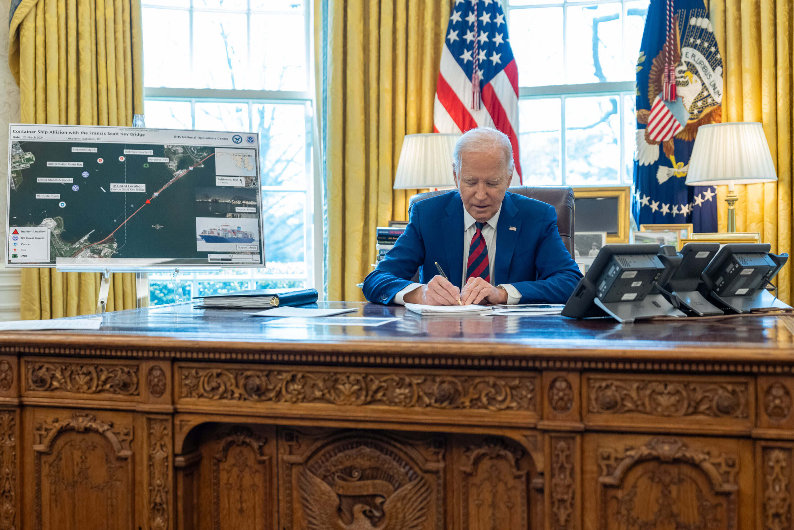 President Joe Biden works at his desk Wednesday in front of a map of the Port of Baltimore and bridge accident. (White House Photo)