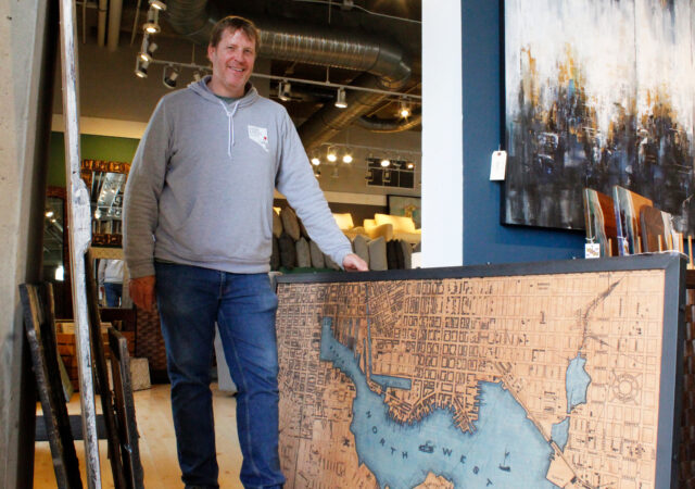 Nicholas Johnson of Su Casa Furniture stands next to a plywood art piece