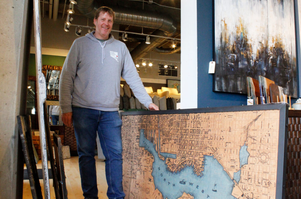 Nicholas Johnson of Su Casa Furniture stands next to a plywood art piece