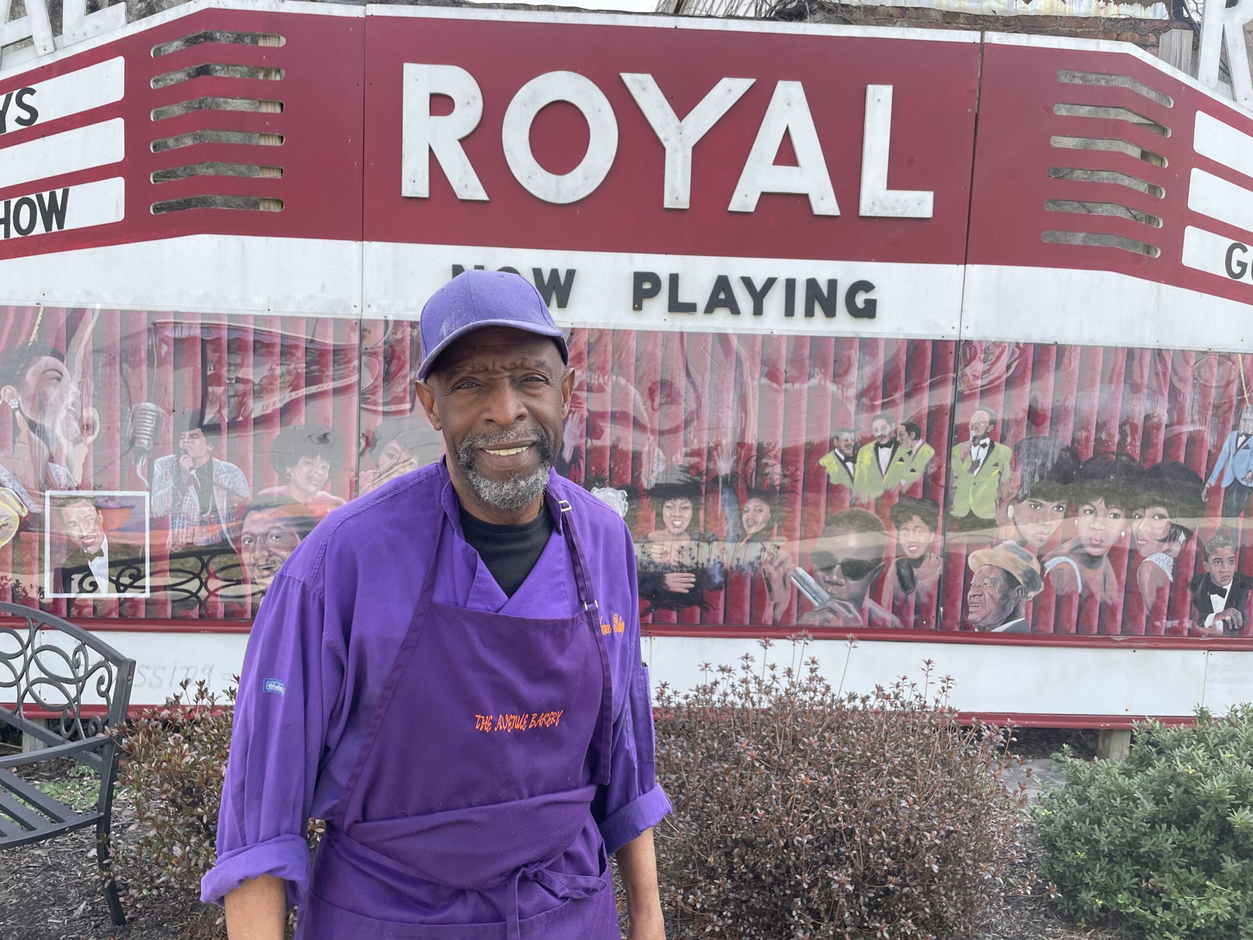 James Hamlin, owner of The Avenue Bakery located on Pennsylvania Avenue, standing in front of a "Royal Theatre" mural outside of his bakery.