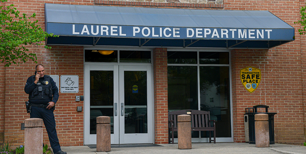 Officer Monarrez takes a call in front of the Laurel Police Department. The building material is made from bricks, and the “Laurel Police Department” is made visible in large font on an awning over the main doors. A sign reading “Safe Place” is also visible on the building.