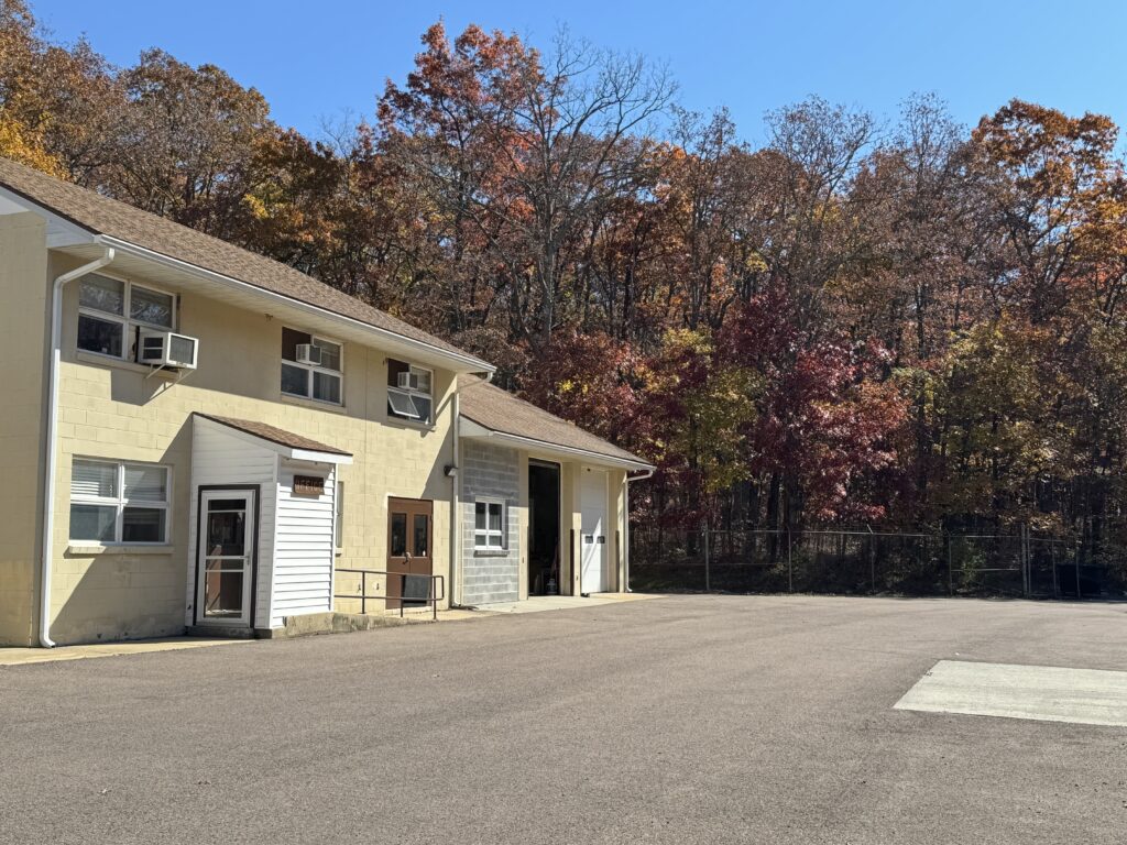 A beige building with garage in front of fall-colored leaves.