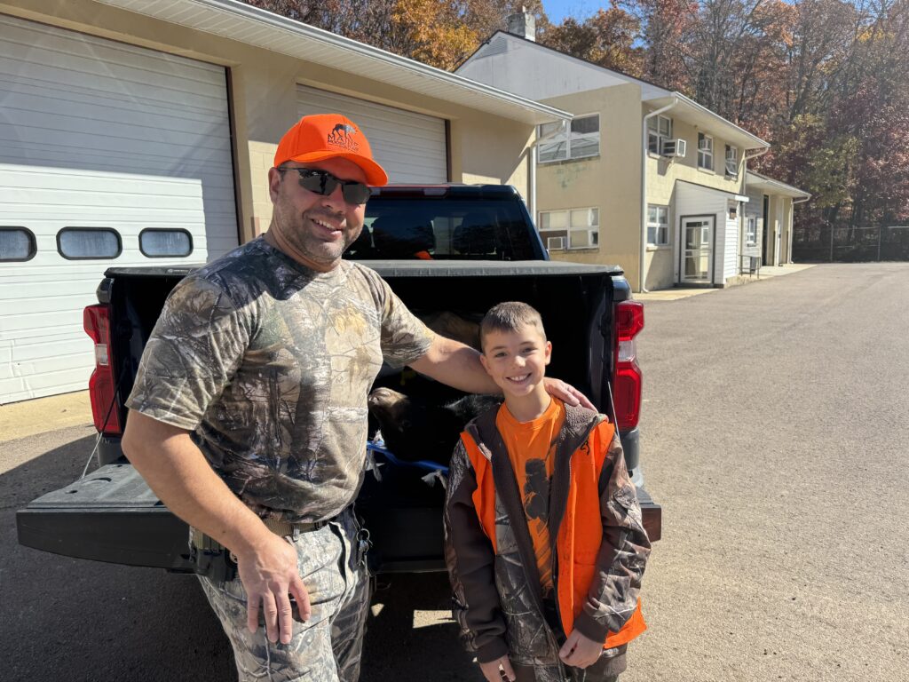 Man and boy in front of pickup truck with a bear they killed for the hunt. 