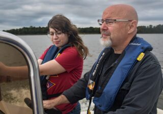 Theaux Le Gardeur and Andrea Rudai are on a motorboat on the Gunpowder River on an overcast day. Le Gardeur is at the helm.