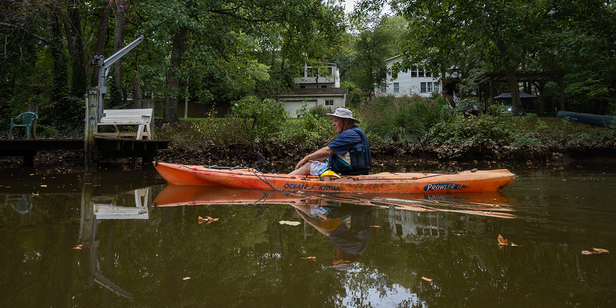 Bill Temmink kayaking on the Gunpowder River with houses and trees in the backdrop.