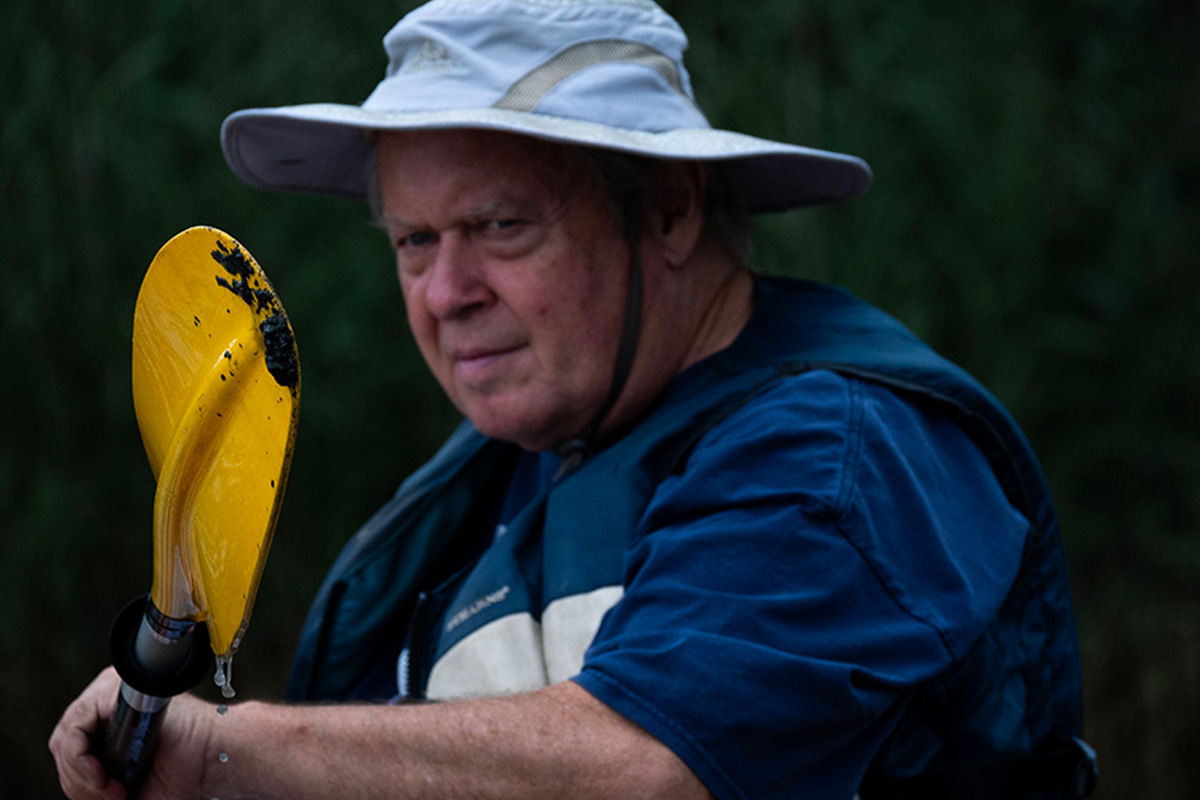Bill Temmink showing the mud he dredged up from the Gunpowder River on his yellow kayak paddle.