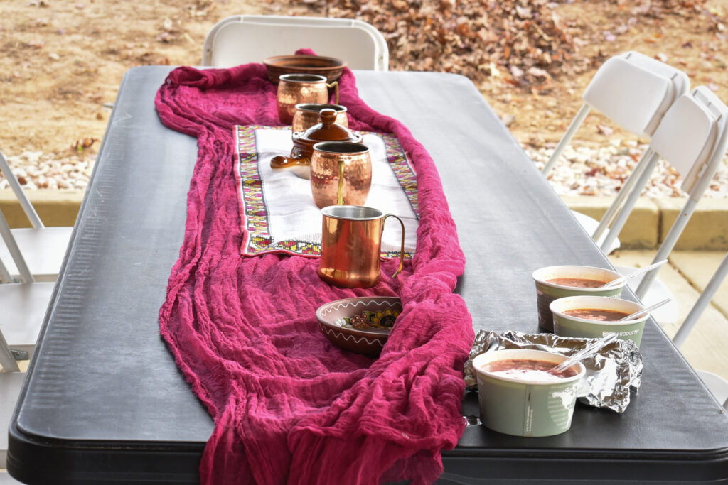 A table with a pink table runner, copper crockery, and three bowls of soup