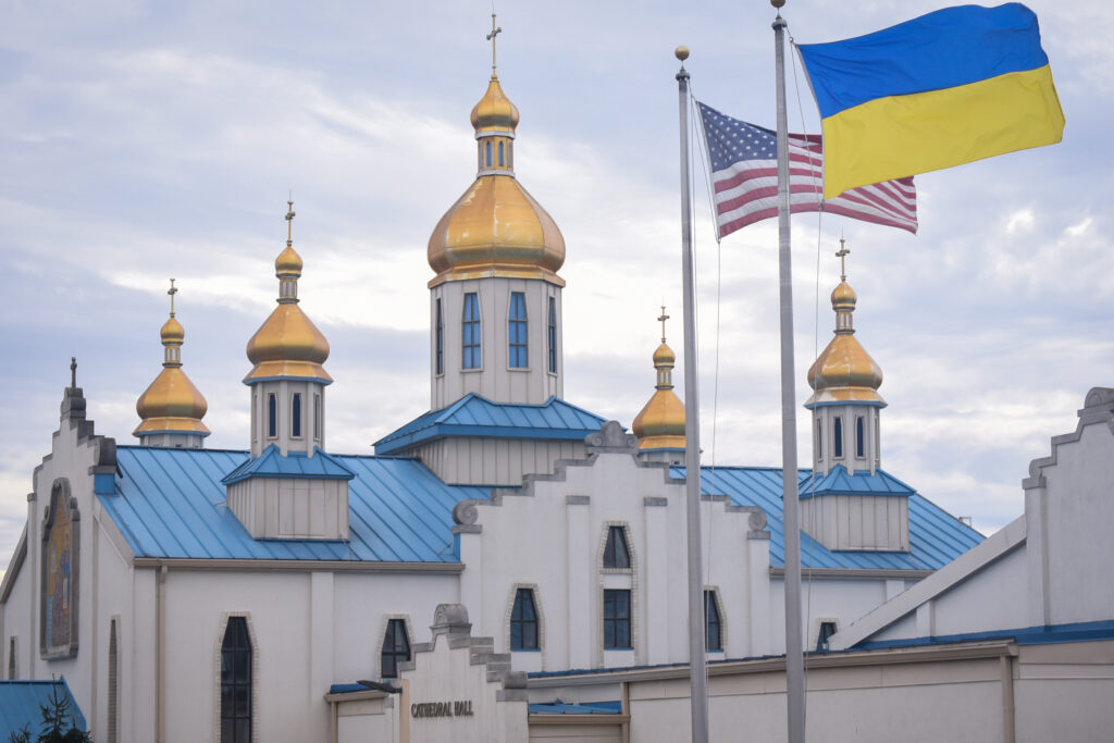 An orthodox church with an American flag and Ukrainian flag flying in the foreground.