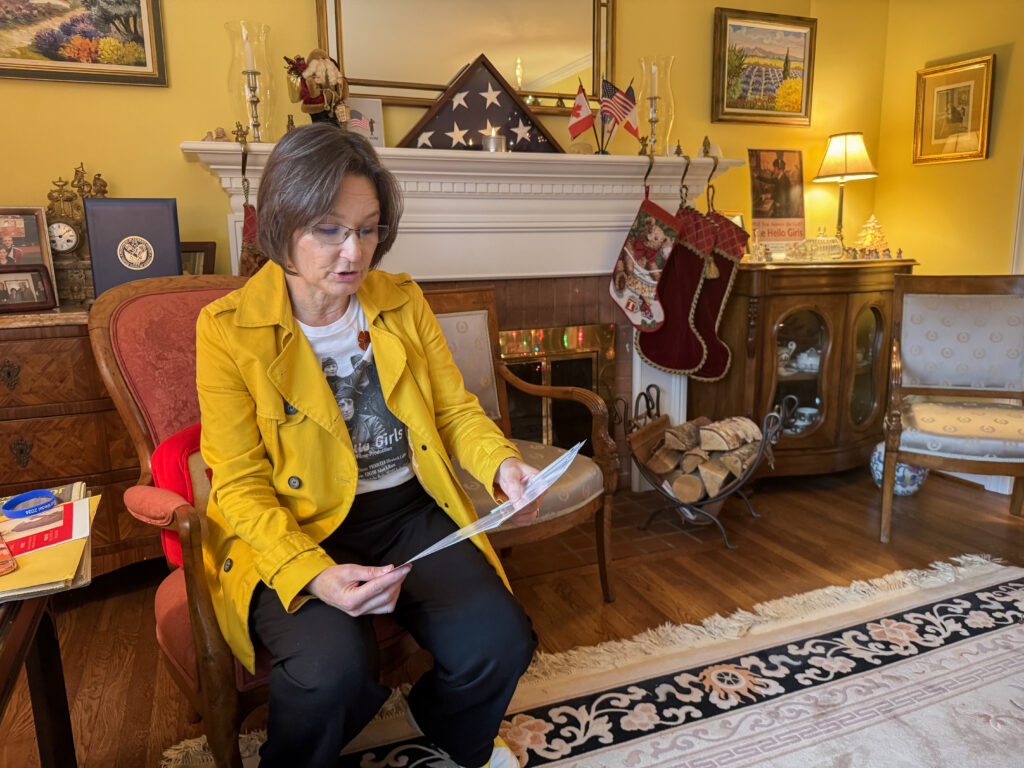 Woman sits in her sitting room reading from a piece of paper.