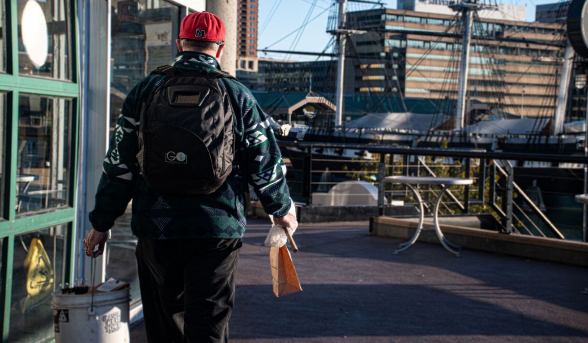 Jon Merryman carries an overflowing bucket filled with rescued birds, while holding a brown bag with another rescued bird, and net, as he continues his walk in Baltimore