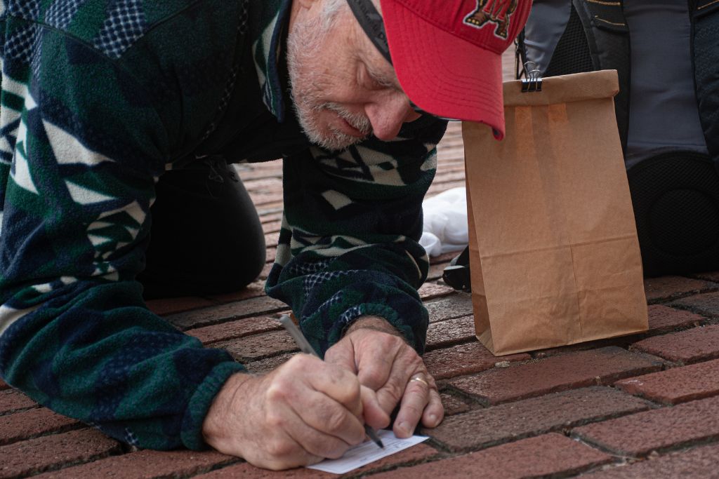 Jon Merryman kneels on the ground, preparing a label documenting the recent victim of a window strike. The survivor is placed in the brown bag until transported to the Phoenix Wildlife Center, where it will receive medical care before being released.