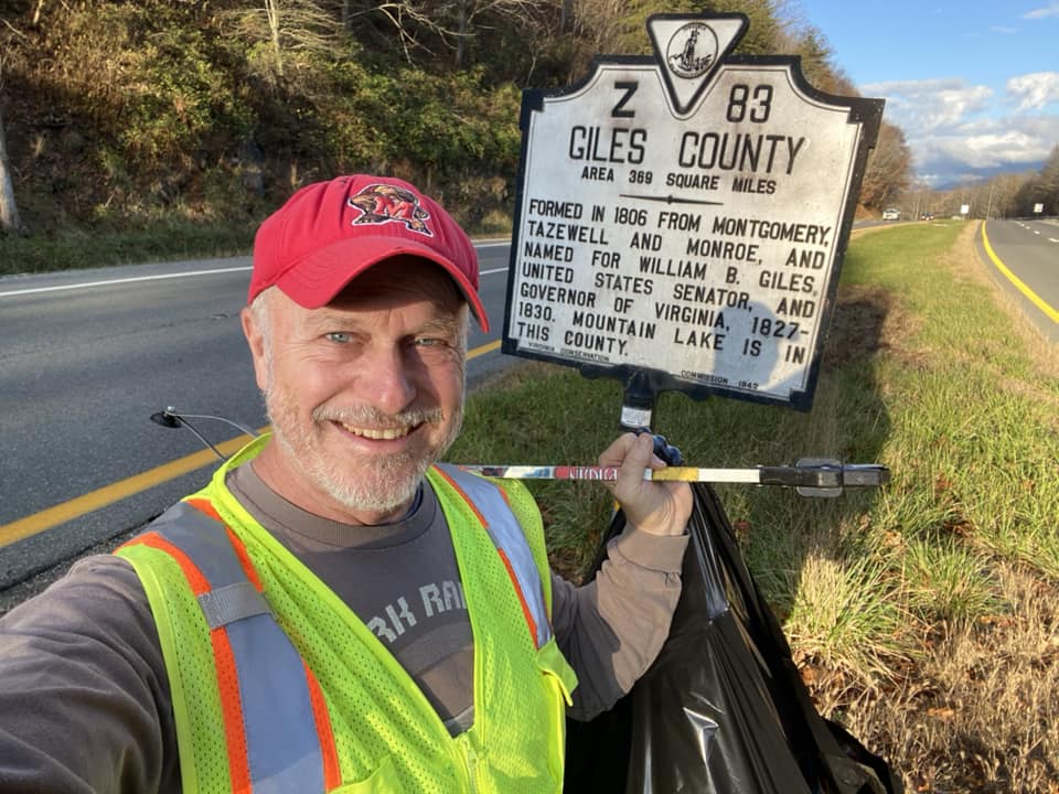 Jon Merryman stands in front on a sign reading, 