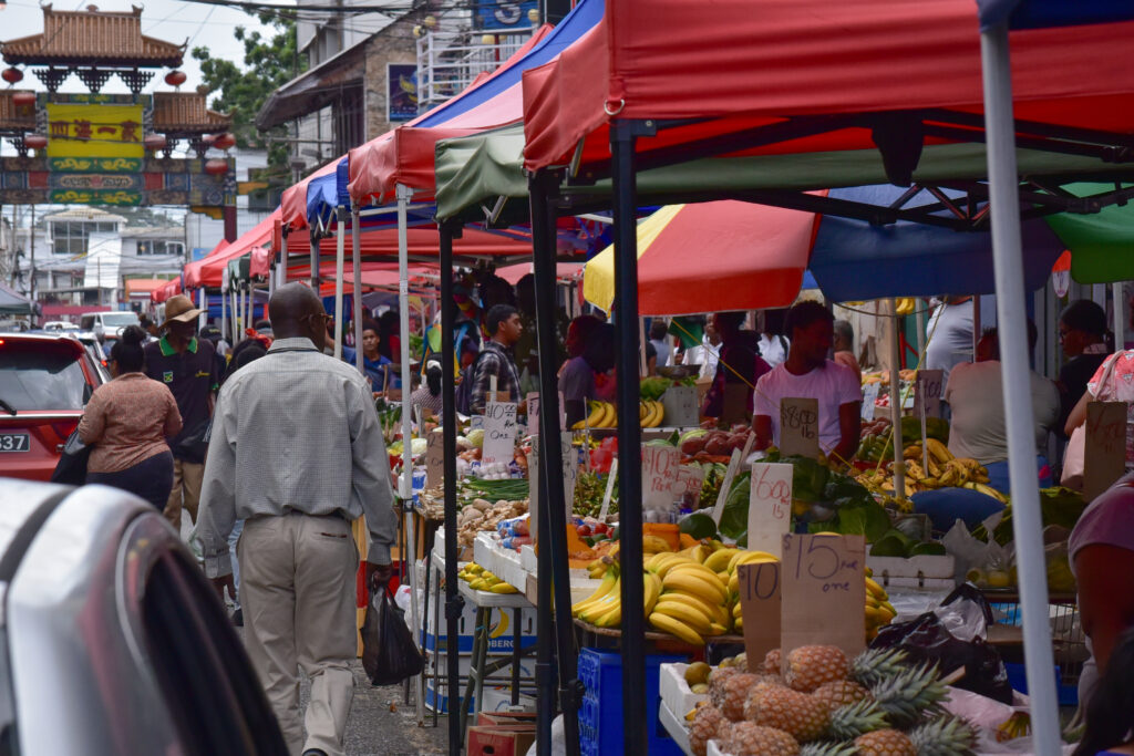 People walk around in a busy market district full of fruit and vegetable stands.