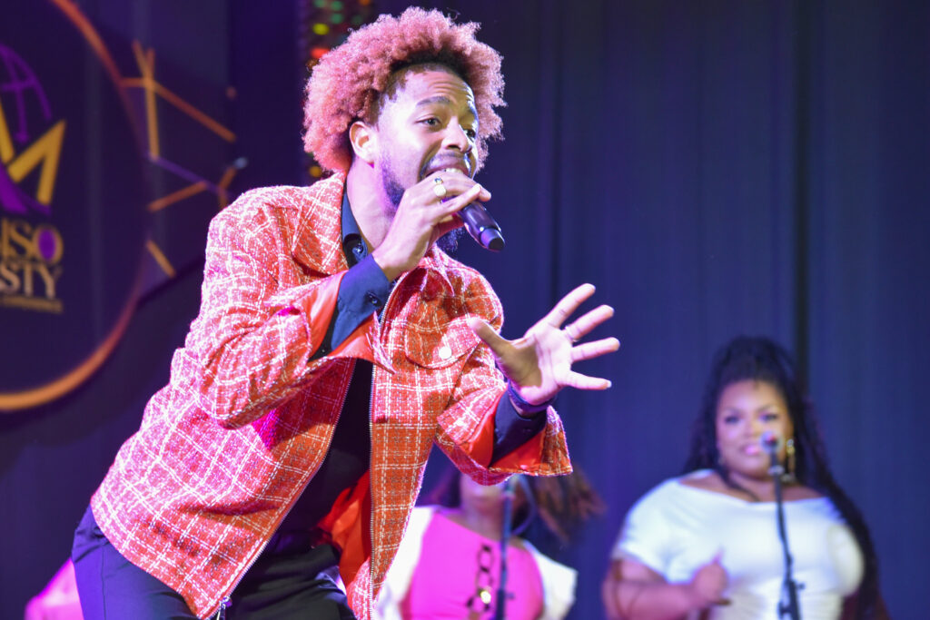 Man sings in front of background singers on a stage.