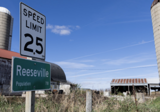 Reeseville’s population sign boasts a modest 718 people, in front of the Statzs’ farm and cows. (Cat Murphy / Howard Center for Investigative Journalism)