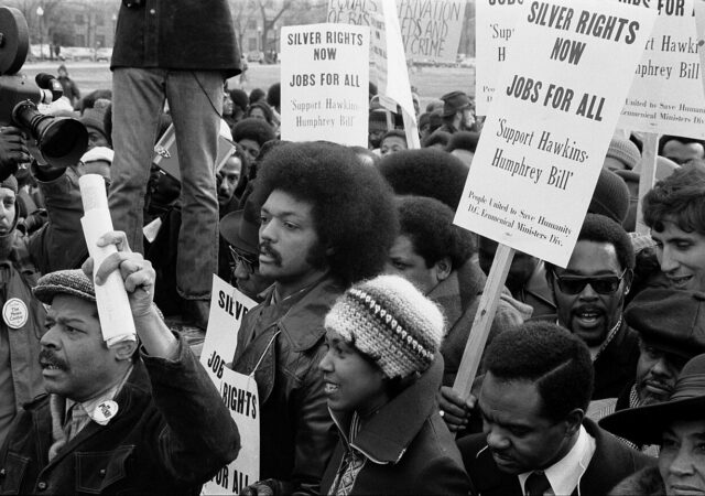 Jesse Jackson surrounded by marchers carrying signs advocating support for the Hawkins-Humphrey bill, in Washington, D.C., in 1975. (Photo by Thomas J. O'Halloran)